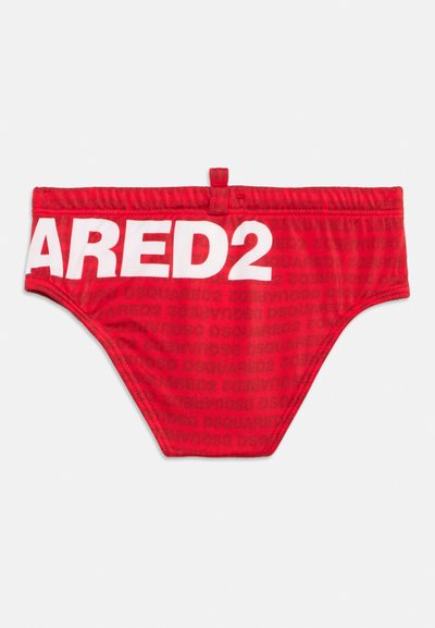 Κόκκινα μαγιό σορτς με θηλιά στη μέση και μεγάλο λευκό κείμενο "ARED2" μπροστά, με φόντο διακριτικό επαναλαμβανόμενο μοτίβο.