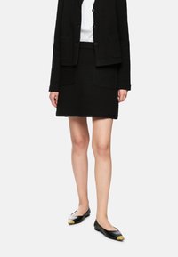 Black textured blazer with matching mini skirt; white blouse underneath. Black flats feature metallic gold and silver toe accents.