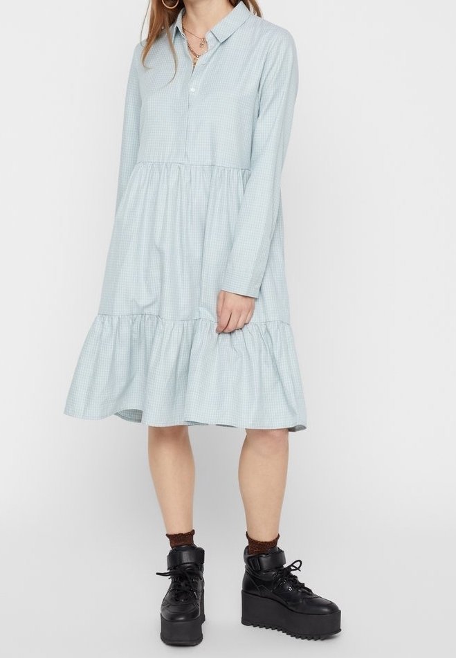 Femme portant une robe bleu clair à manches longues à volants avec col, associée à des bottines noires à plateforme à lacets et des chaussettes sombres jusqu'aux chevilles.