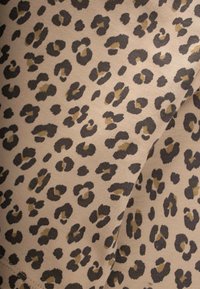 Bēšs audums ar leoparda rakstu, melnas un brūnas plankumi, kas izceļ gludu tekstūru un mīkstu izskatu.