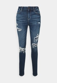 Jeans de denim skinny fit em azul escuro com rasgos desgastados nos joelhos. Apresenta um design clássico de cinco bolsos e fecho com botão na cintura.