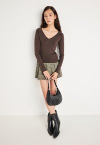 Καφέ μακρυμάνικη μπλούζα με V-ντεκολτέ, πράσινη καρό πτυχωτή φούστα, μαύρες γόβες και μια μαύρη καμπυλωτή τσάντα.