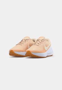 Sneakers sportivi con upper in mesh di un leggero pesca, presentano un logo swoosh bianco, colletto imbottito e suola in gomma arancione testurizzata.