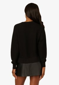 Maglione nero lavorato a maglia con vestibilità morbida, maniche lunghe e orlo a costine. Abbinato a una gonna mini in pelle nera elegante.