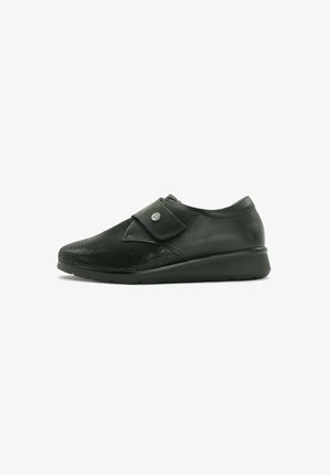 Zapato negro con parte superior de cuero texturizado y lados lisos, que presenta una correa de Velcro y un diseño de punta redondeada, asentado sobre una suela baja y resistente.