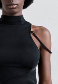 Top negro sin mangas con cuello alto, que presenta un detalle único en las tiras de los hombros y una textura de tela suave. Corte ajustado con costuras mínimas.