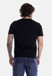 Maglione nero a maniche corte in maglia con orlo a coste e scollatura rotonda, abbinato a jeans in denim blu che presentano un classico design con tasca posteriore.