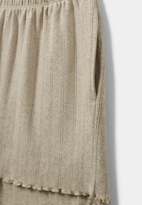 Svetlo bež pletena suknja s okomitim prugama i teksturiranim uzorkom. Ima elastičnu traku u struku i volanastu donicu, te bočnu džep.