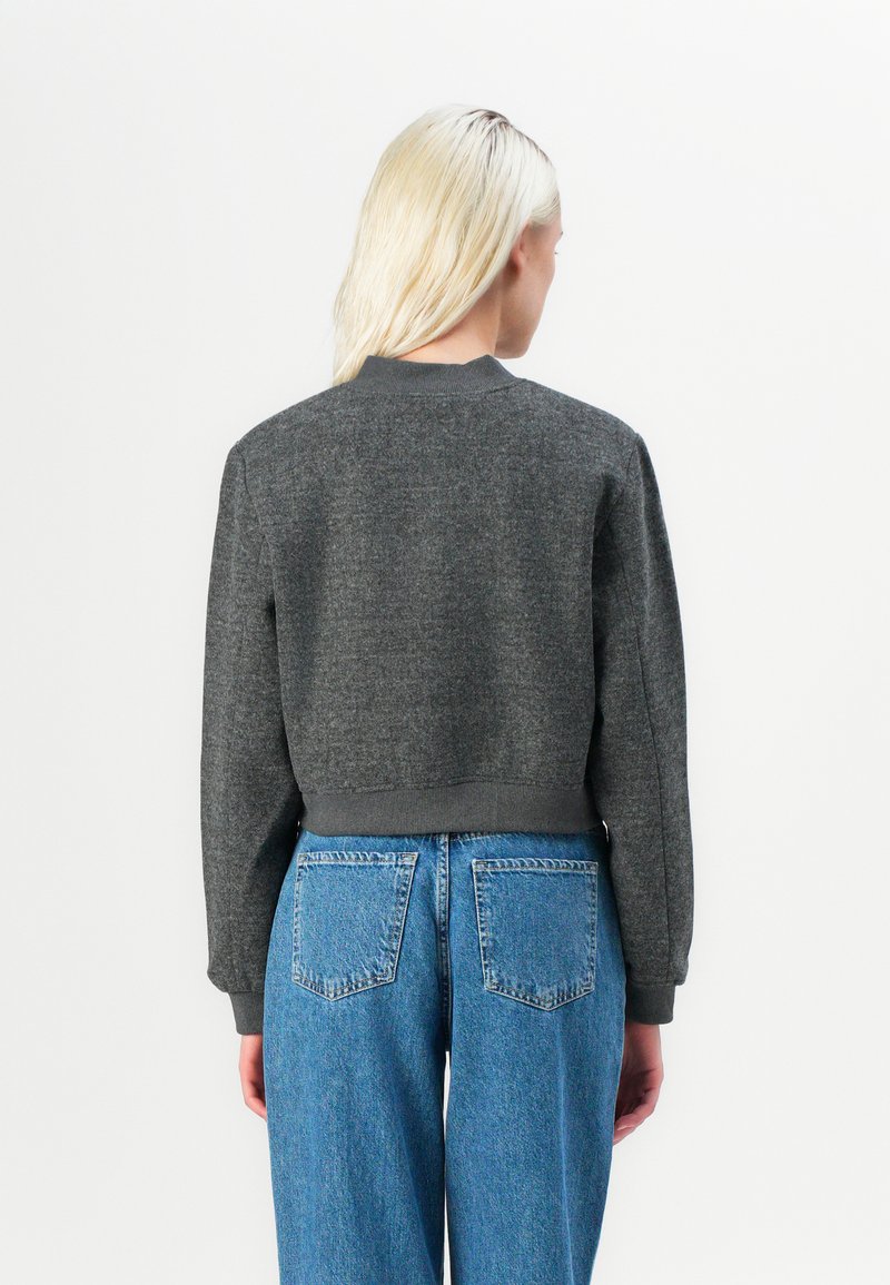Sweatshirt gris court avec col et poignets côtelés, fabriqué en tissu doux. Associé à un jean en denim bleu taille haute avec poches arrière.