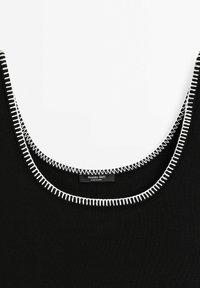 Haut noir sans manches avec des surpiqûres blanches en zigzag autour de l'encolure dégagée et une étiquette de marque visible à l'intérieur du col.