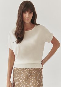 White short-sleeve sweater with a round neckline and a ribbed hem, paired with a brown skirt featuring a light abstract pattern.