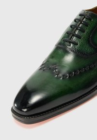 Green leather shoe featuring a glossy finish, pointed toe, decorative stitching, and textured accents near the laces.
