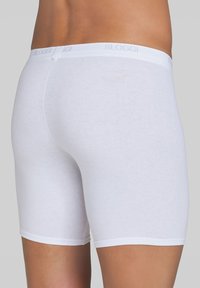 Boxer shorts bianchi in cotone con una consistenza morbida e liscia e una cintura elastica che mostra il nome del marchio "SLOGGI". Lunghezza a metà coscia.