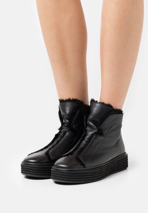 Botas de tobillo de cuero negro con un acabado texturizado, paneles laterales elásticos y un ribete de piel sintética; cuentan con una suela gruesa y estriada para mayor altura.