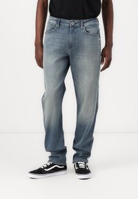 Lichtblauwe denim jeans met een rechte snit, voorzien van een klassiek vijf-pocket ontwerp en een lichte vervagingseffect, gecombineerd met zwarte sneakers.