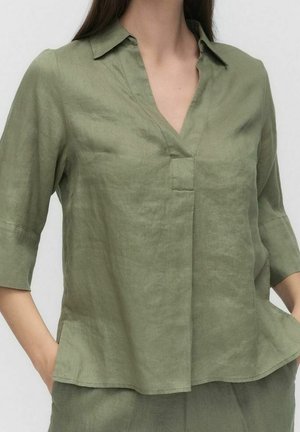 Oliivivihreä pellavapusero, jossa on V-pääntie, lyhyet hihat ja etutasku. Ominaisuutena rento leikkaus ja hieman teksturoitu pinta.