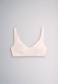 Soft pale pink wireless bra with wide straps and a deep scoop neckline laid flat on light gray background.