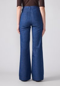 Ψηλόμεσοι φαρδυίοι τζιν παντελόνια σε μπλε απόχρωση με λεία υφή, διαθέτοντας δύο πίσω τσέπες και καθαρή ραφή.