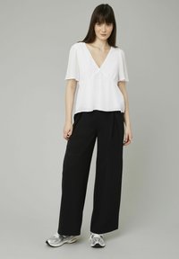 Blouse blanche texturée avec un décolleté en V et des manches courtes, accompagnée de pantalons larges noirs taille haute et de chaussures de sport argentées.