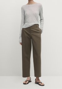 Haut à manches longues gris en tissu léger, associé à un pantalon droit taille haute de couleur vert foncé. Des sandales plates noires complètent le look.