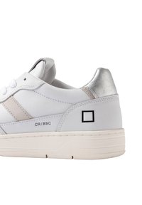 Hvide sneakers med en glat læderoverdel, lys grå accenter, sølvhælhætte og et sort firkantet logo. Polstret krave og flade snørebånd.