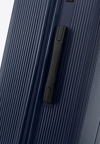 Valigia rigida blu navy con texture a righe verticali, dotata di maniglia nera e cerniera, realizzata in materiale sintetico durevole.