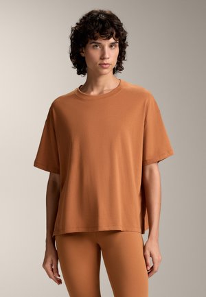 Loose-fitting, short-sleeve t-shirt in a warm orange-brown color made of soft fabric, featuring a round neckline and a straight hem.