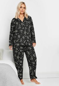 Conjunto de pijama negro con estampado floral blanco, parte superior de botones de manga larga y pantalones a juego. Tejido suave, corte relajado y diseño de pierna recta.