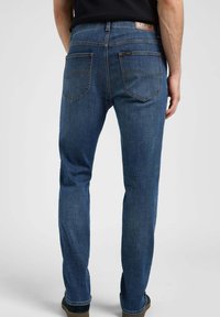 Vaqueros de mezclilla en un tono azul oscuro, con corte recto, diseño de cinco bolsillos, costuras sutiles, y parche de cuero con marca en la cinturilla.