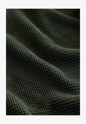 Tissu texturé vert foncé avec un motif en nid d'abeille, comportant des carrés doux et surélevés ainsi qu'un drapé légèrement ondulé.