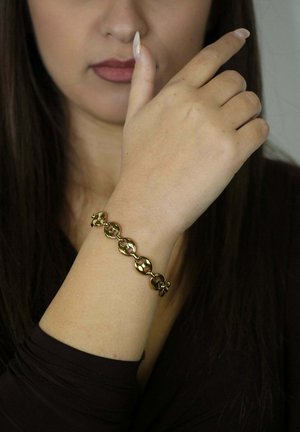 Bracciale a catena d'oro con maglie ovali, caratterizzato da una finitura lucida. Indossato su un polso, mette in risalto il design del bracciale e la sua texture liscia.