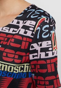 Camiseta de malla con una base negra y estampados de texto y logotipo multicolores, escote redondo y mangas cortas. Textura suave y diseño atlético.