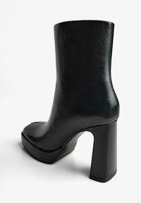 Gheată neagră cu toc înalt, din piele netedă, cu vârf pătrat, toc gros și un design elegant cu accente minime.