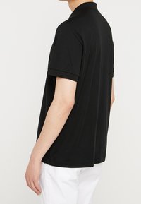 Polo noir présenté de dos, en coton doux, avec des manches courtes, un col classique et une coupe droite au niveau de l'ourlet.