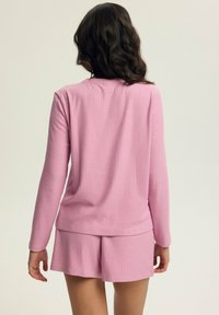 Różowa, prążkowana bluzka z długim rękawem w komplecie z pasującymi szortami. Miękka faktura, luźny krój i prosty brzeg. Brak widocznych wzorów lub elementów metalowych.