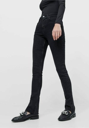 Jean skinny noir en denim avec poches avant et taille haute. Doté d'une fermeture par boutons, de passants pour ceinture et de détails de couture contrastants.