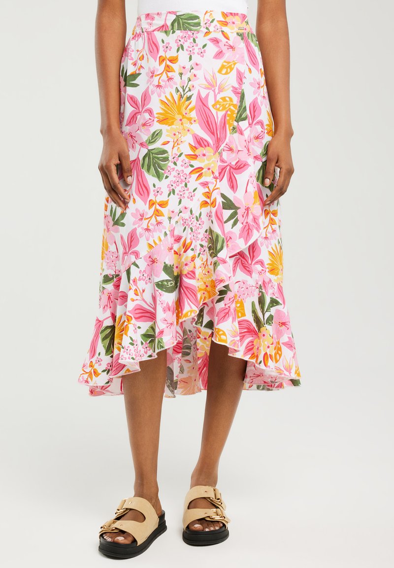 Jupe midi florale présentant des motifs roses, jaunes et verts, avec un ourlet à volants et en tissu léger. Associée à des sandales beiges.