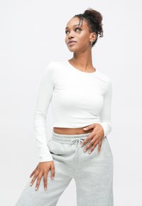 Hvid langærmet cropped top med rund halsudskæring, kombineret med grå joggingbukser med elastisk talje og snøre.