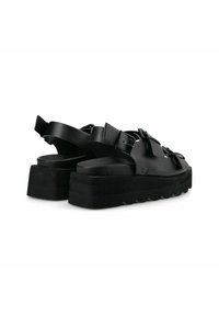 Sandalias de plataforma negras con una suela gruesa, que cuentan con correas ajustables y un acabado elegante y suave. Los detalles notables incluyen hebillas y una suela texturizada.