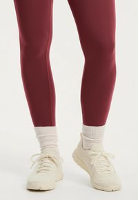 Vinröda leggings i slät tyg, figurnära design, kombinerade med gräddvita ankelsockor och lätta gräddvita sneakers med texturerade ytor.