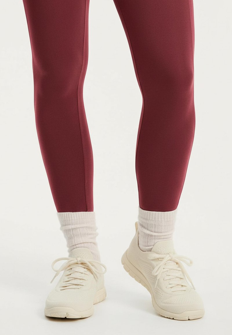 Vinröda leggings i slät tyg, figurnära design, kombinerade med gräddvita ankelsockor och lätta gräddvita sneakers med texturerade ytor.