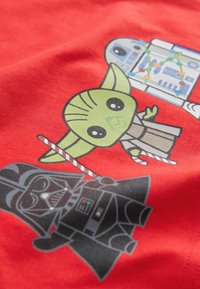 Červené bavlněné tričko s kreslenými postavičkami: zelený Yoda, modrý R2-D2 a černý Darth Vader, s detaily na jejich kostýmech.