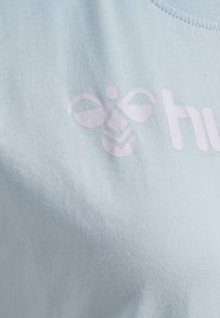 Hellblaues Baumwoll-T-Shirt mit rundem Halsausschnitt und einem glänzenden rosa Logo mit abstrakten Formen auf der Vorderseite.