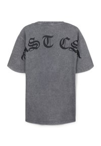 T-shirt grigio oversize con bold lettering nero "MSTCS" sulla schiena. Realizzato in cotone con una finitura morbida e texturizzata.