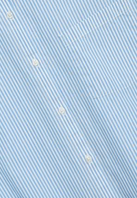 Camicia a righe azzurro chiaro e bianca in tessuto leggero, con taschino applicato e bottoni bianchi lungo la parte anteriore.