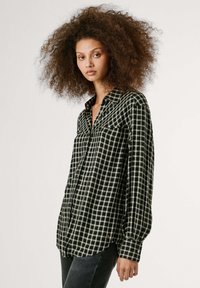 Camicia a scacchi nera e verde con colletto button-down, maniche lunghe e orlo curvo. Il tessuto appare morbido, con una texture liscia.