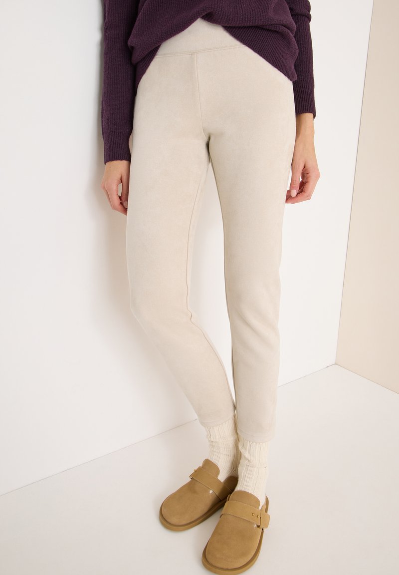 Pantaloni elasticizzati beige realizzati in un materiale morbido con una texture liscia; abbinati a zoccoli color cammello e calzini a coste di colore crema.