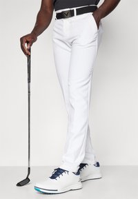 Balti golfai su elegantišku dizainu, derinami su baltais ir tamsiai mėlynais sportbačiais. Golferis laiko juodą putter'į su tekstūruota rankena.