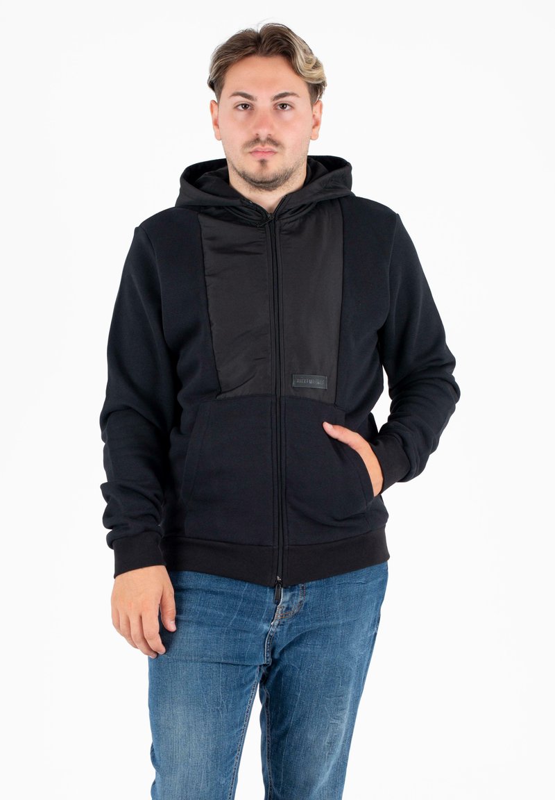 Felpa nera con zip, dotata di un pannello in raso di contrasto sul fronte, due tasche laterali e cappuccio con cordino. Polsini e orlo aderenti.