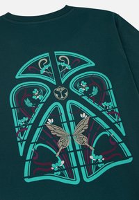 Donkergroene sweatshirt met een groot turquoise en kastanjebruin grafisch ontwerp van gestileerde bloemen en een vlinder, gedetailleerd met ingewikkeld lijnwerk.